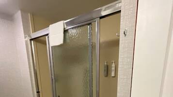 A bathroom with a glass shower enclosure, a white door, and a trash can.