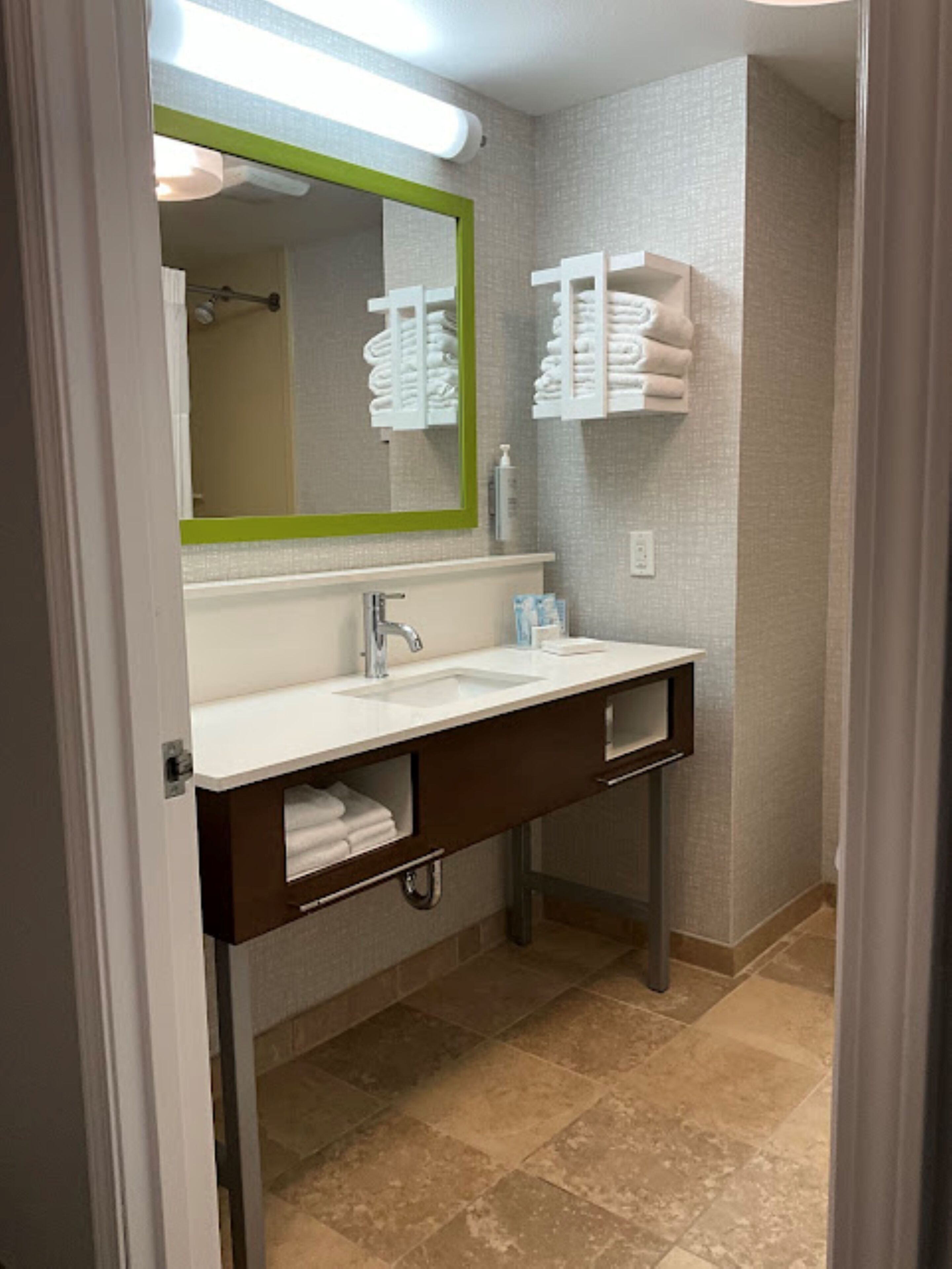 A bathroom with a white sink, a green-framed mirror, and towel racks on the wall.