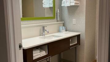 A bathroom with a white sink, a green-framed mirror, and towel racks on the wall.