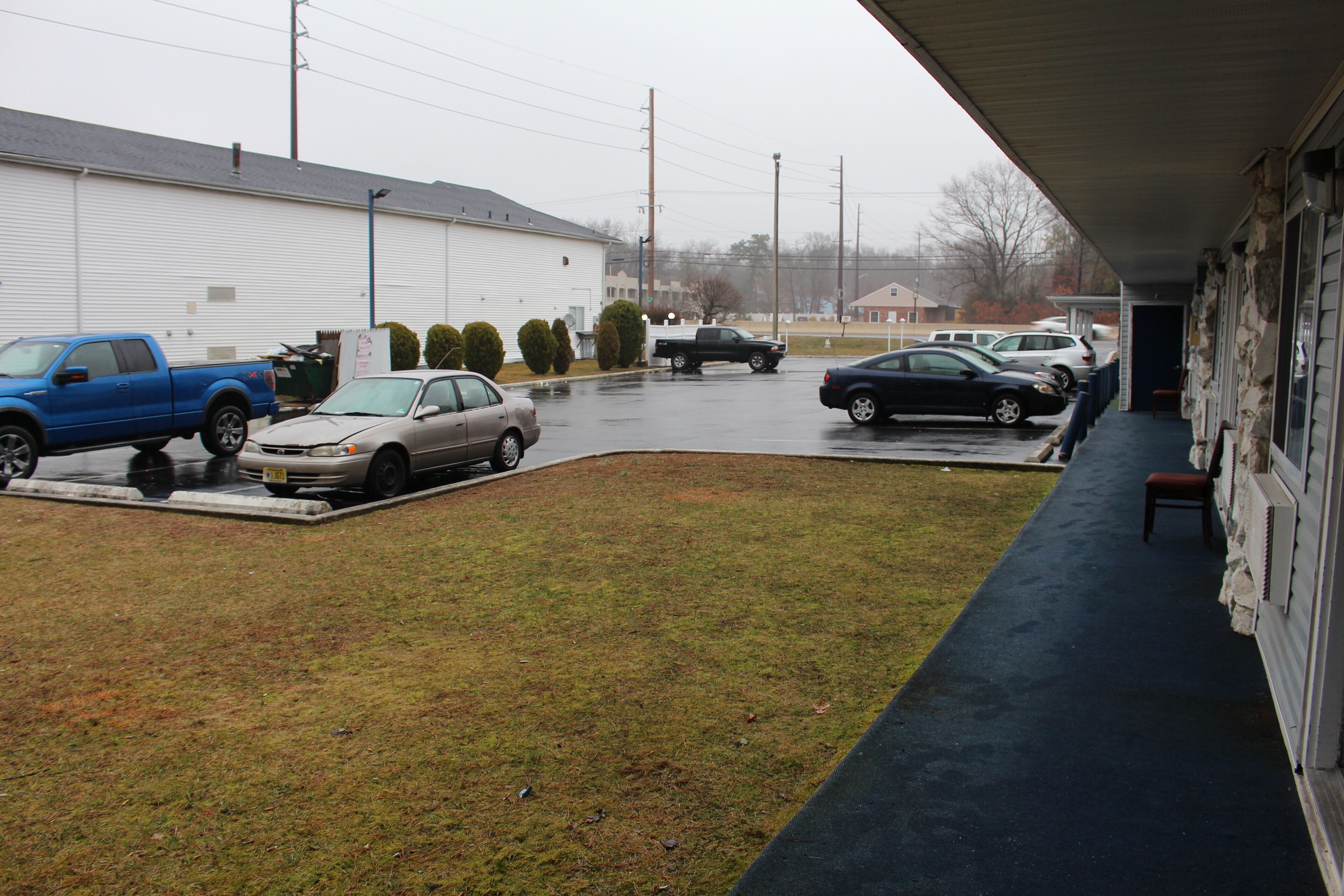 A parking area with several cars, a building with a covered porch, and a grassy lawn.