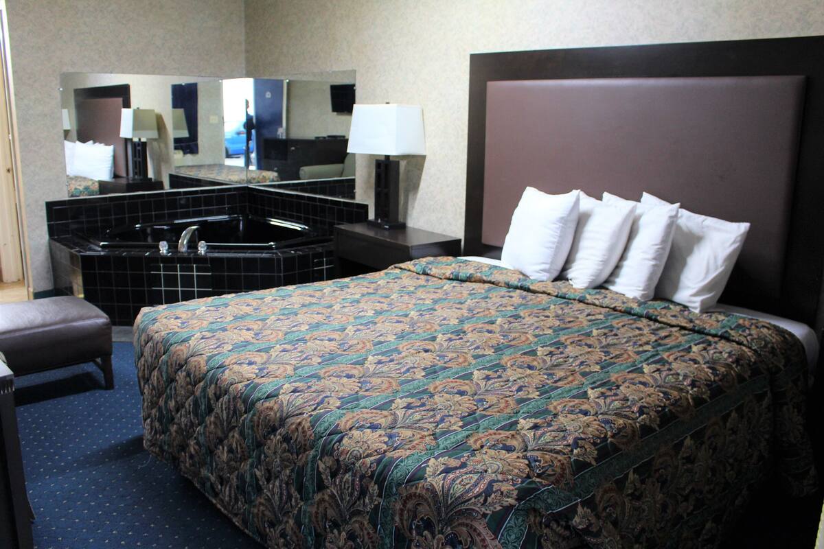 A hotel room with a large bed, a bathroom with a bathtub, and a mirror.