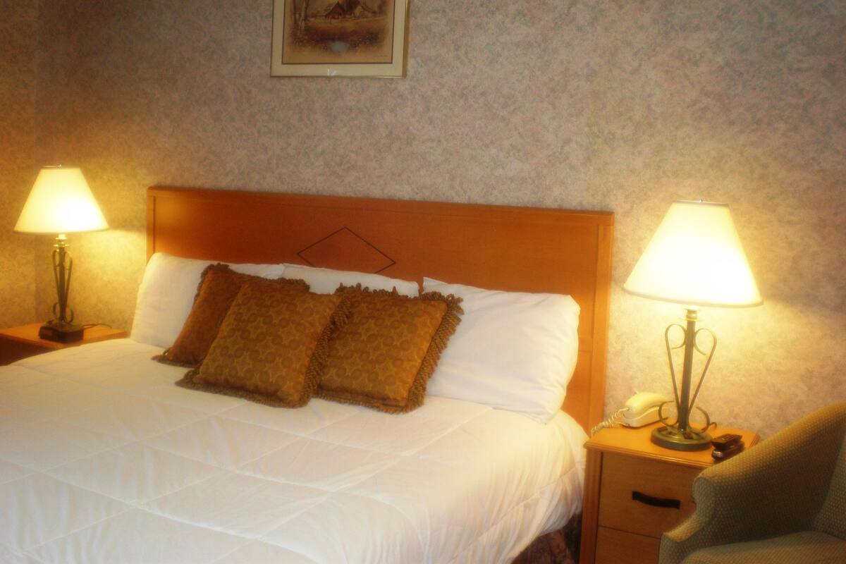 A neatly made bed with two pillows, a wooden headboard, and two bedside lamps on either side.