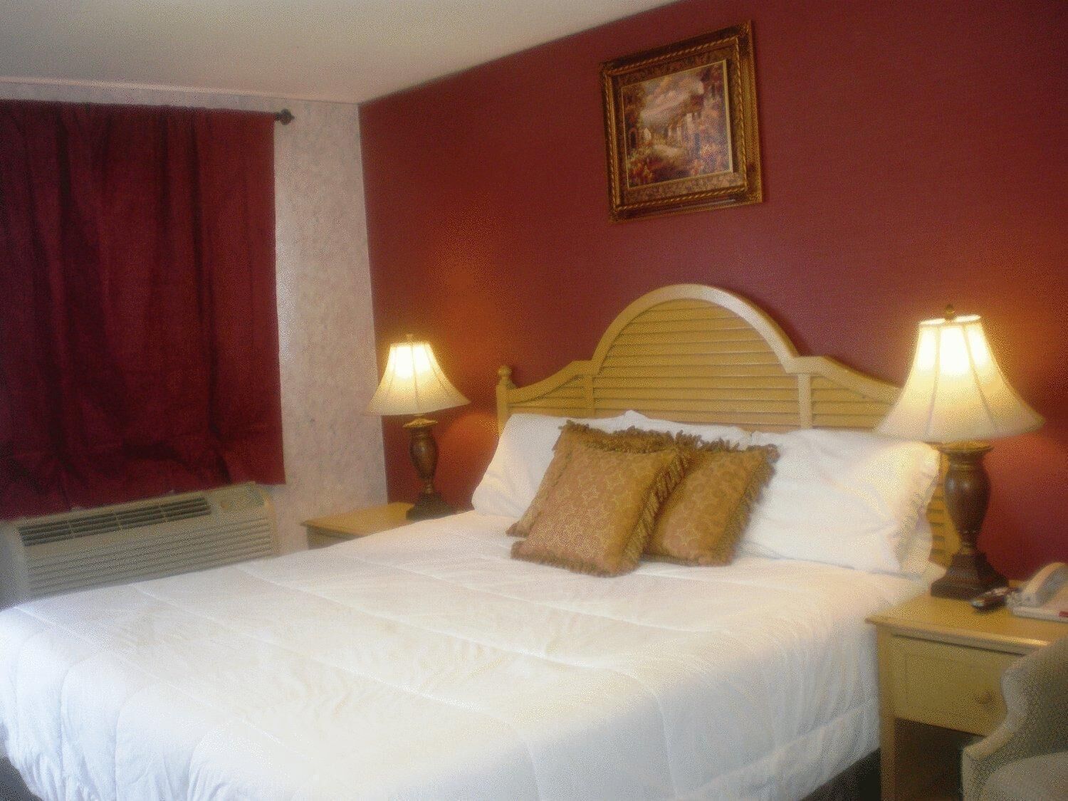 Una cama bien hecha con sábanas blancas, dos lámparas de noche y una cortina roja.