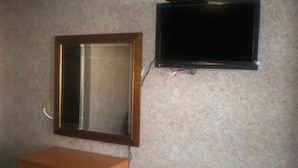 A mirror with a wooden frame, a television mounted on the wall, and a wooden dresser with drawers.