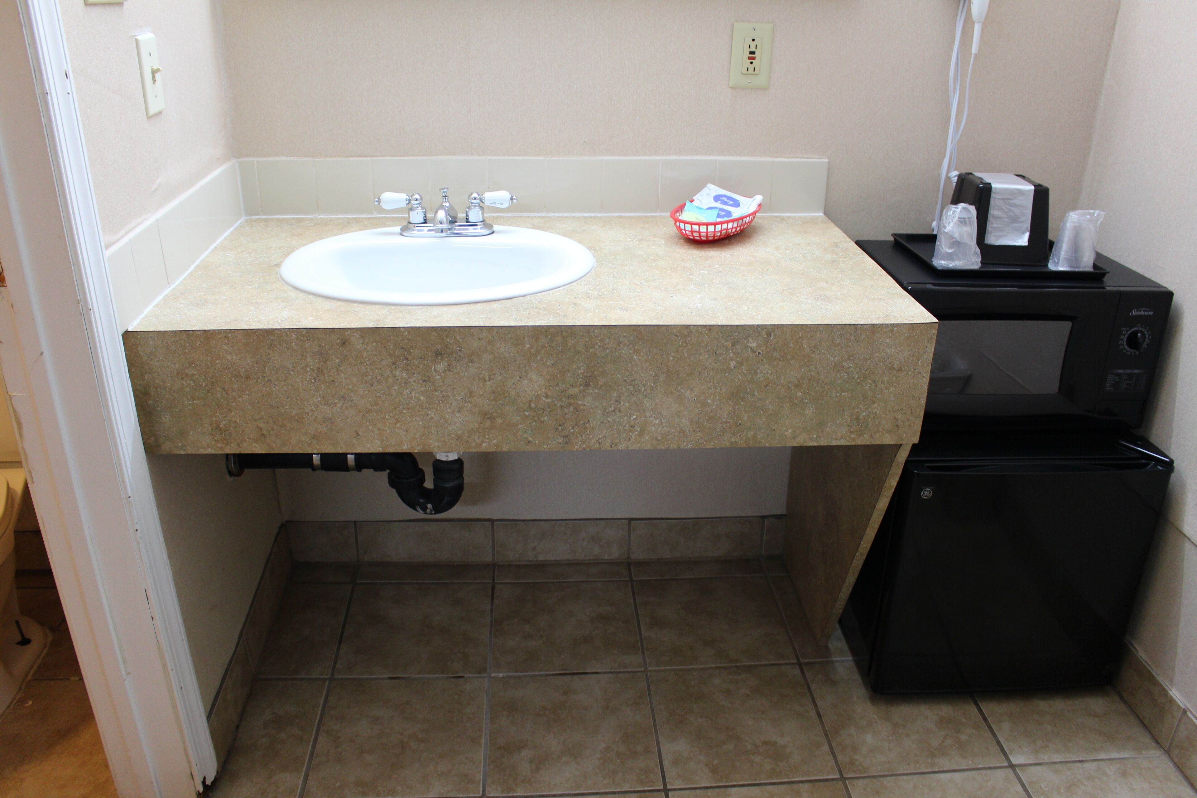 A bathroom with a sink, a microwave, and a small refrigerator.