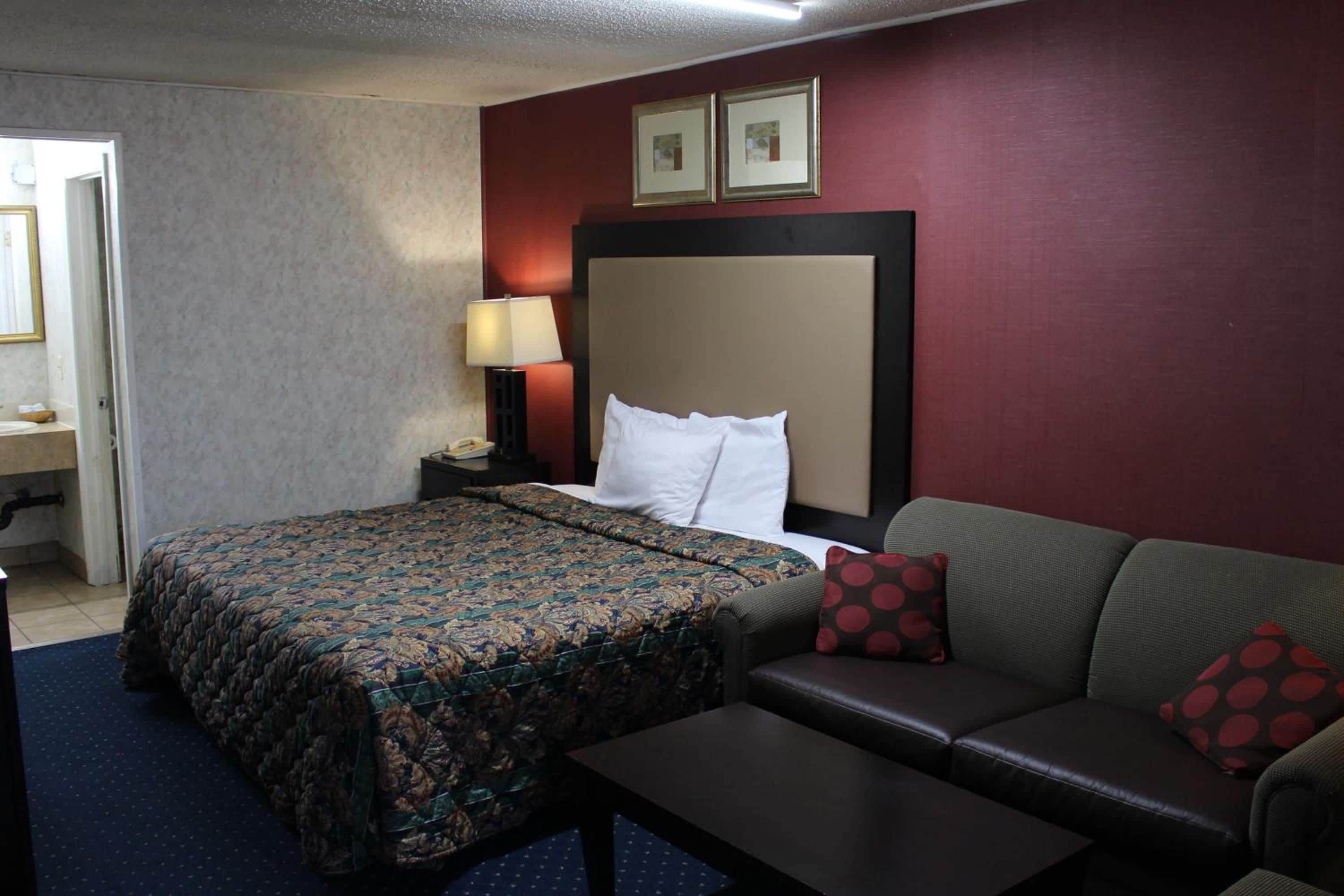 A hotel room with a bed, a sofa, a nightstand with a lamp, and a small table.