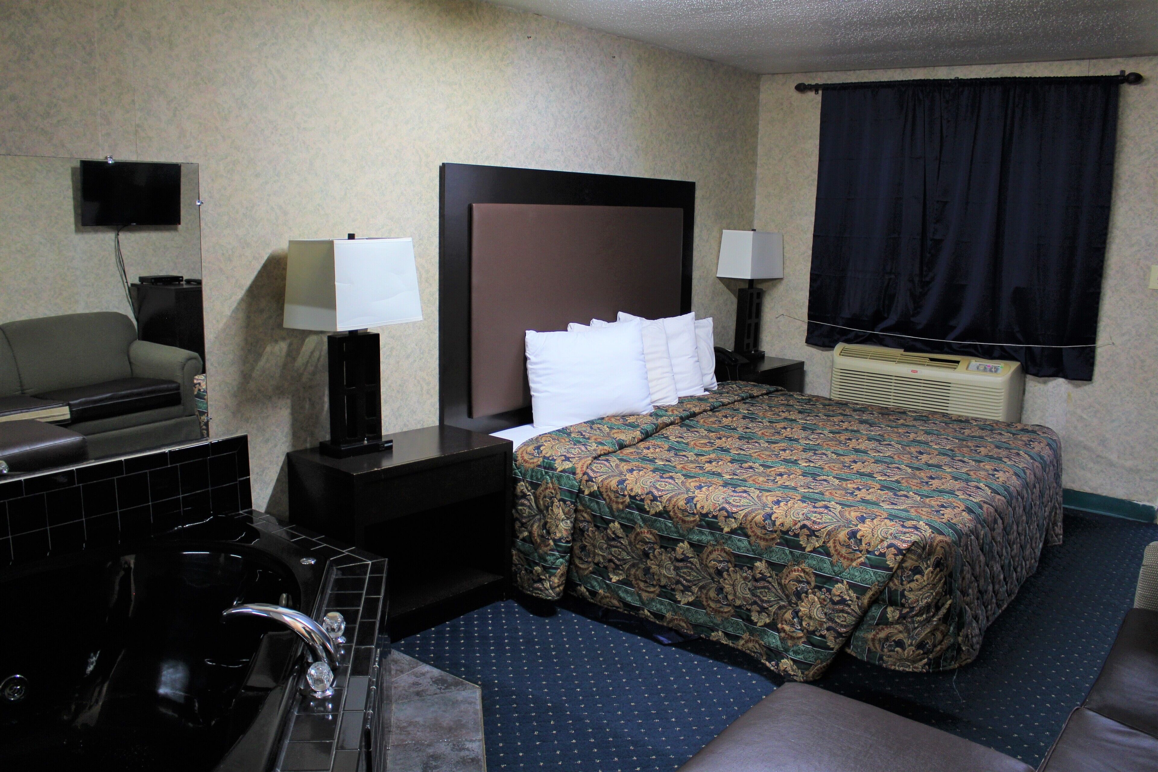 A hotel room with a bed, a sofa, a desk, a TV, a lamp, and a bathroom with a bathtub.