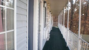 A covered porch with a wooden floor and white railings, leading to a door.