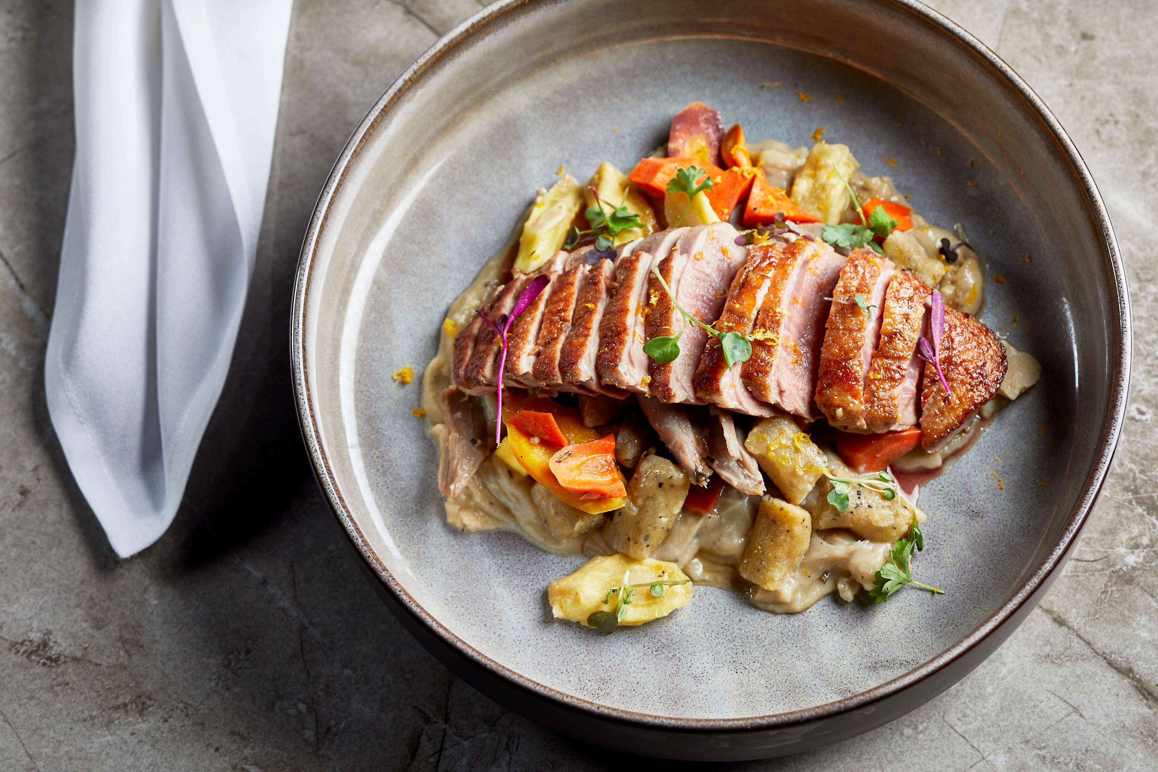 A plate of sliced duck with vegetables and sauce.