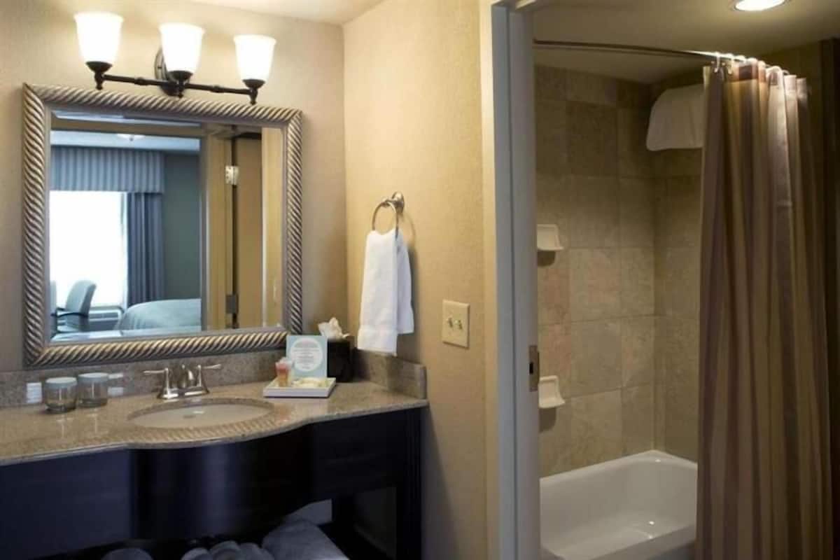 A hotel bathroom with a large mirror, two sinks, a bathtub, and a shower curtain.