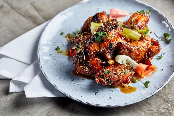 A plate of glazed chicken wings garnished with herbs and vegetables.