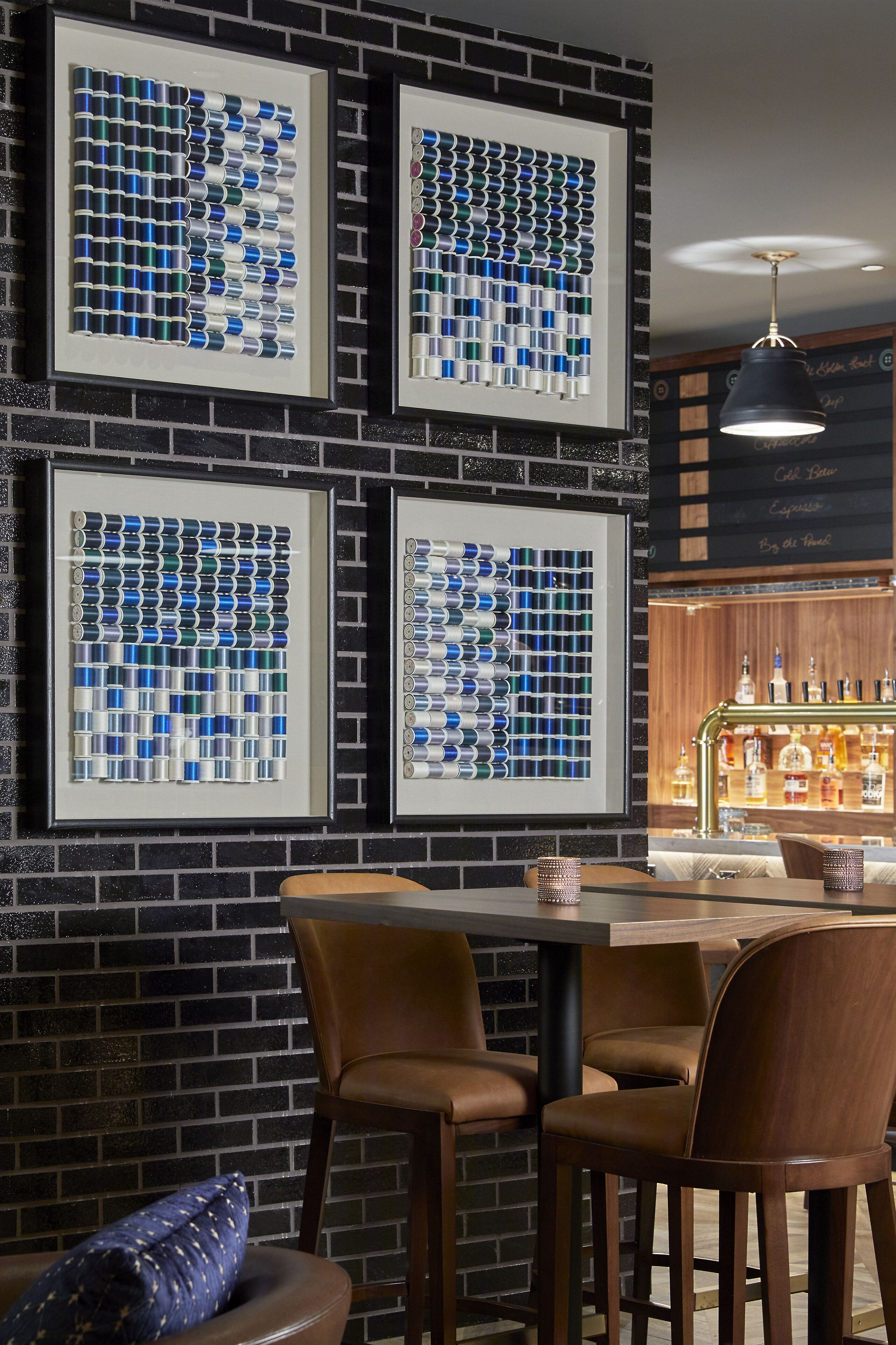 A bar area with framed artworks of blue and white canisters, a dark brick wall, and a wooden bar counter with bottles.