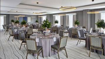 A spacious banquet hall with round tables, chairs, and large floral centerpieces.
