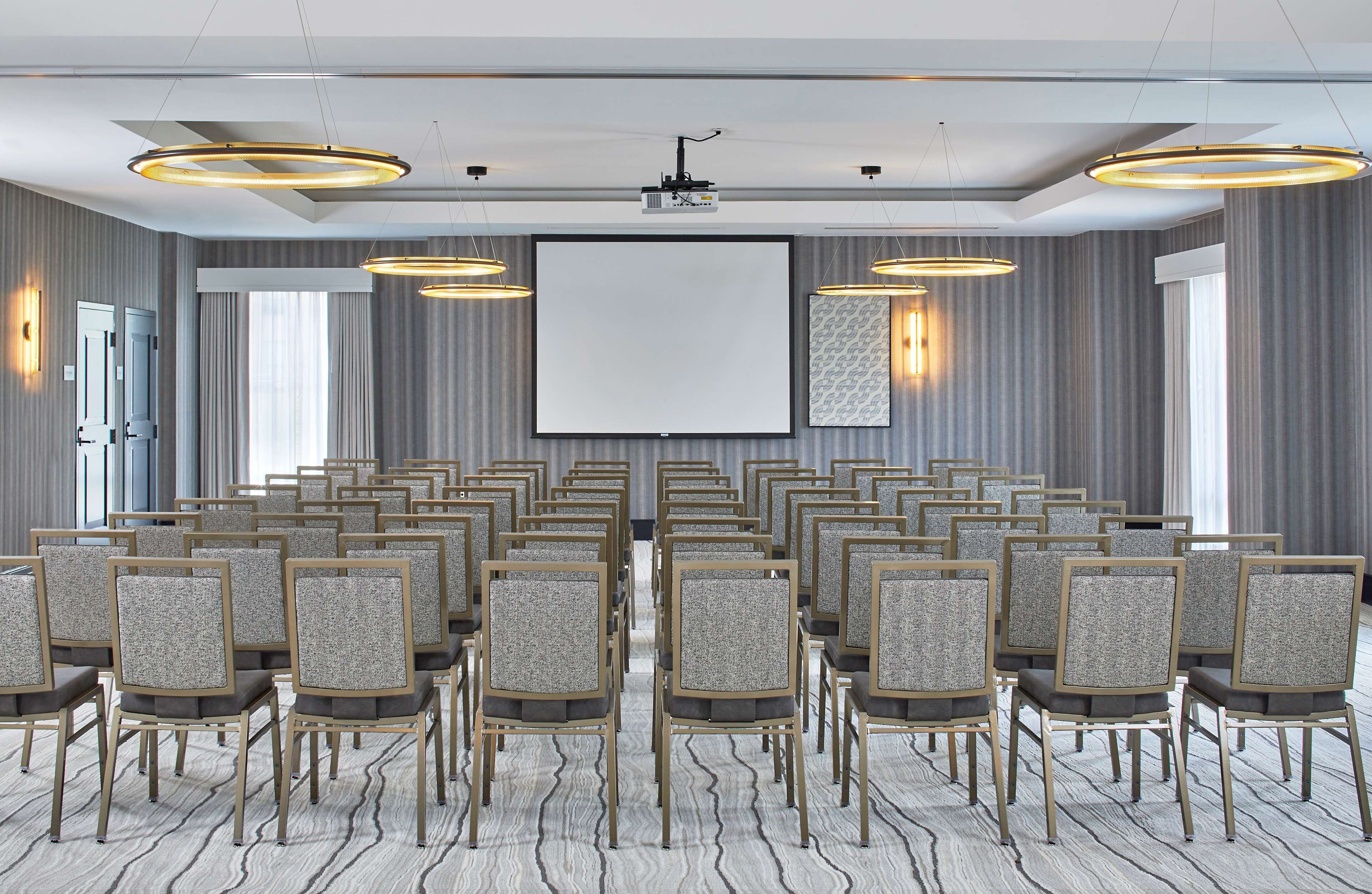 A conference room with rows of chairs, a large screen, and overhead lighting.