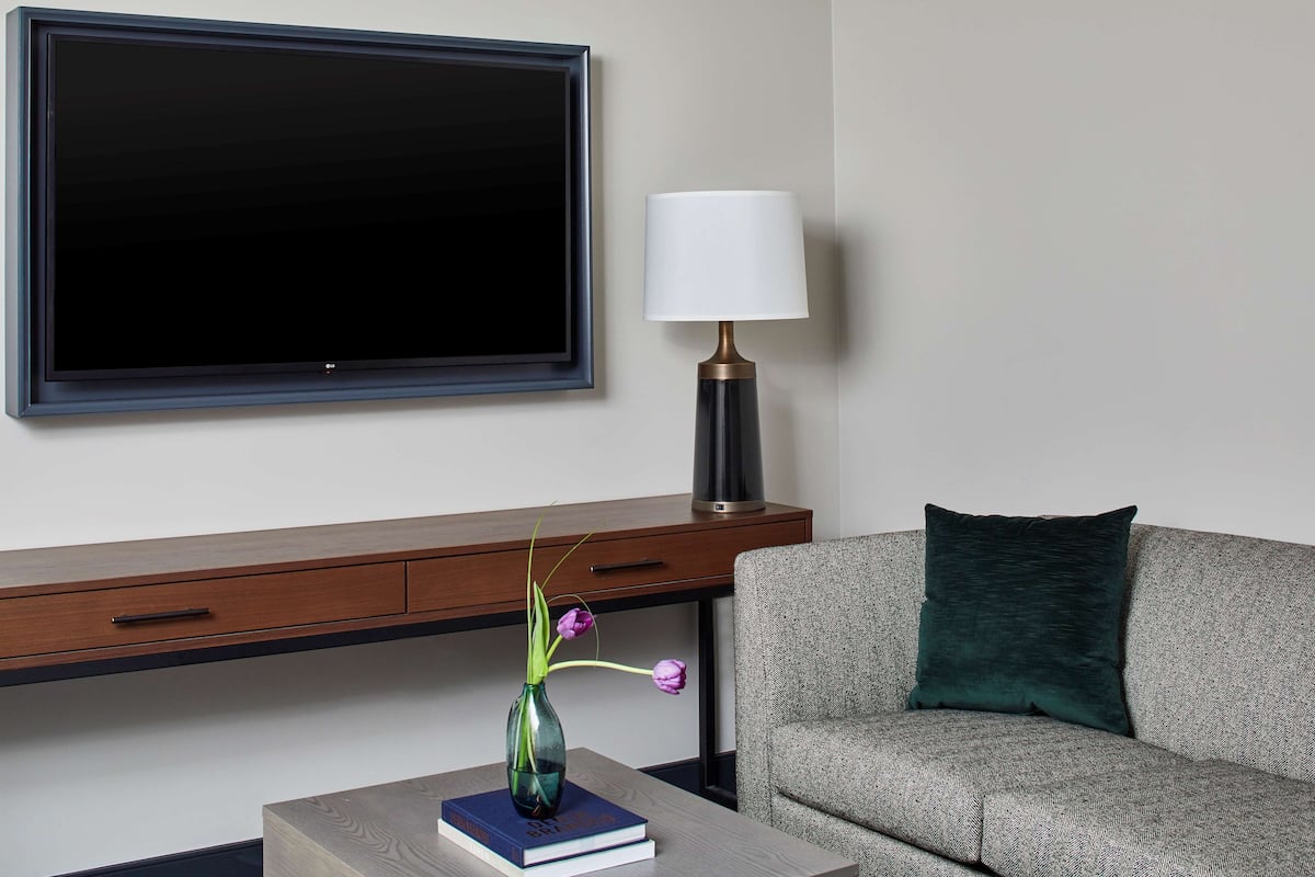 A modern living room with a flat-screen TV, a lamp, a vase with flowers, and a sofa.