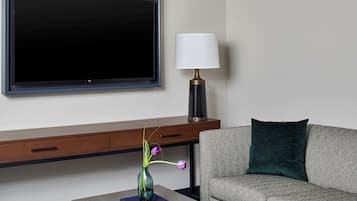 Una sala moderna con una televisión de pantalla plana, una lámpara, un jarrón con flores y un sofá.