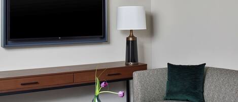 Una sala moderna con una televisión de pantalla plana, una lámpara, un jarrón con flores y un sofá.