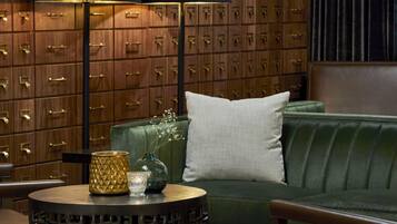 A room with a green sofa, a round table with a vase and a candle, and a wall of wooden lockers.