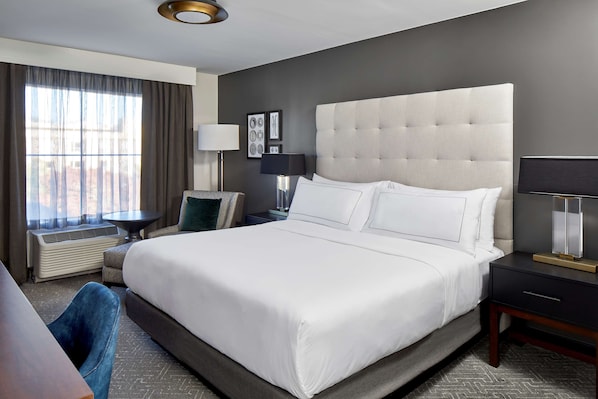 Habitación de hotel con una cama grande, un escritorio, una silla, una lámpara y una ventana con cortinas.