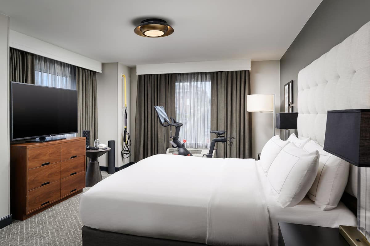 A hotel room with a large bed, a TV, a desk with a lamp, and exercise equipment.