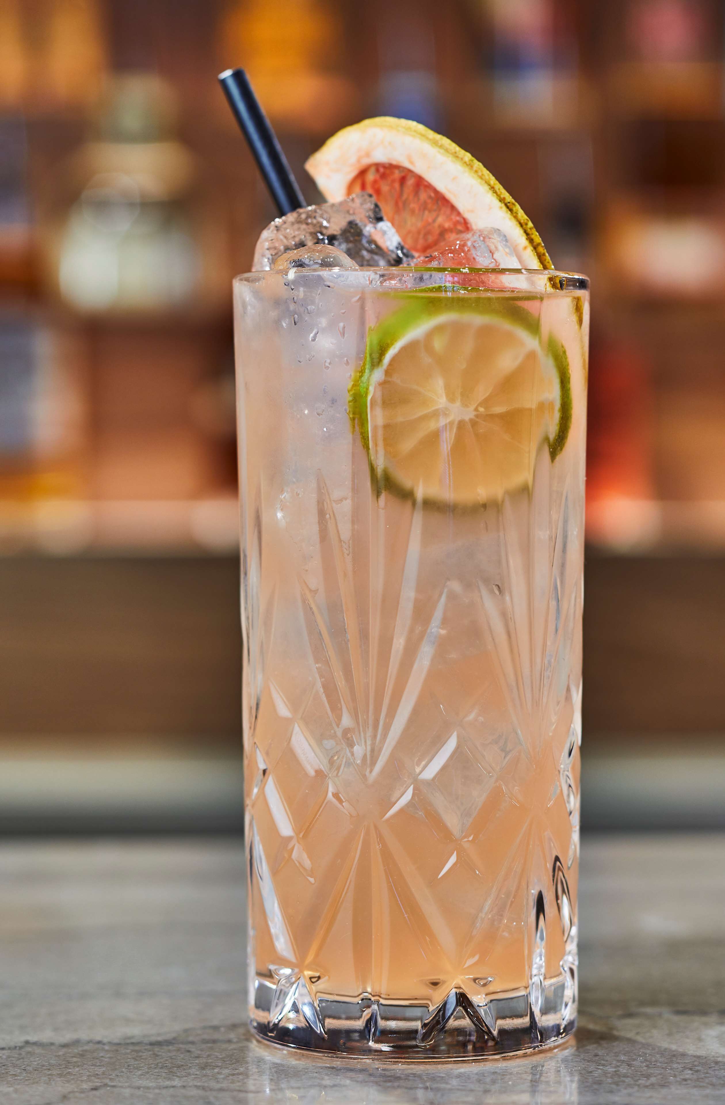 A clear glass with a textured pattern, containing a beverage with ice cubes, a lime slice, and a straw.
