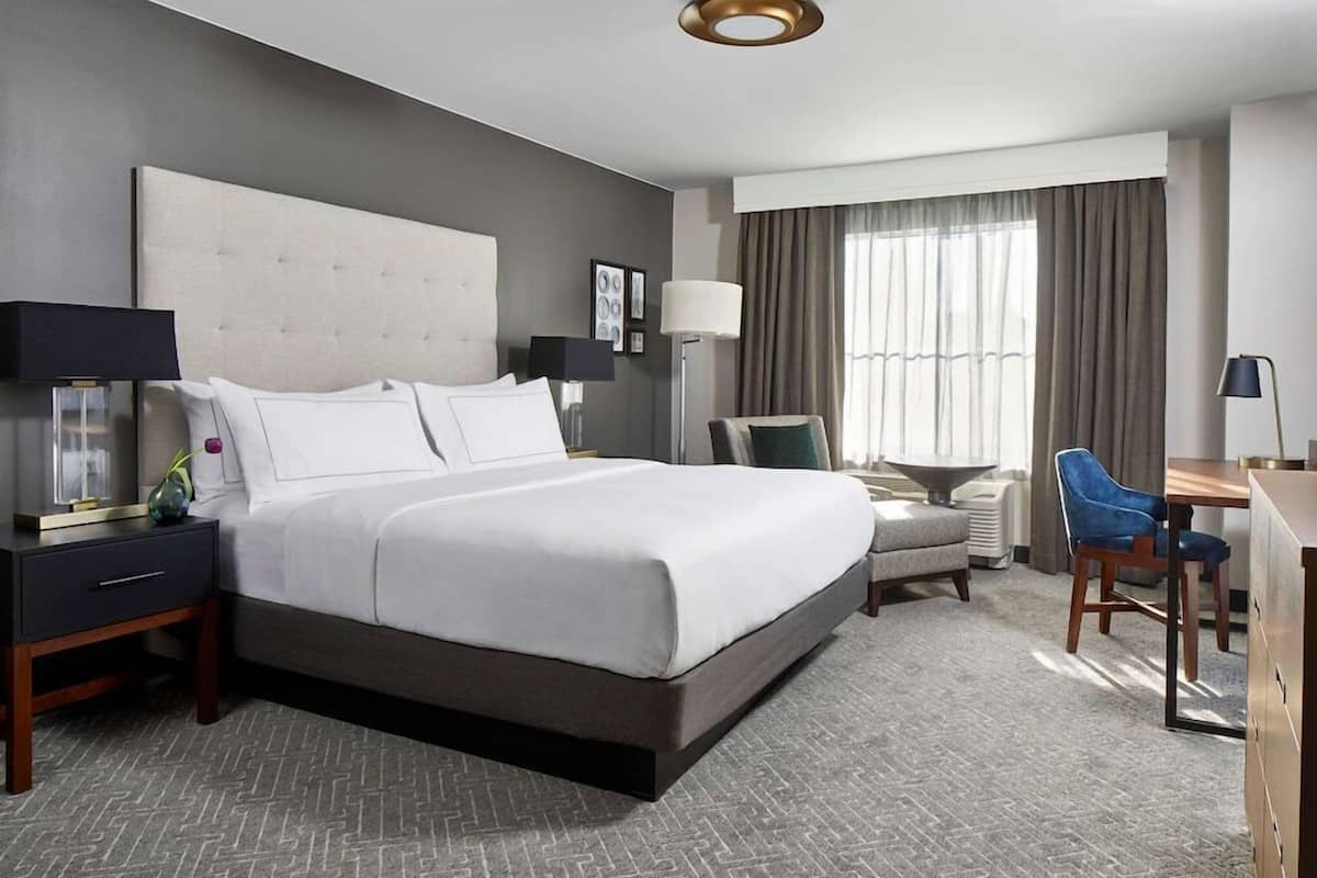 A modern hotel room with a large bed, bedside tables, a desk, and a chair.