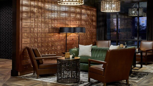 A modern lounge area with leather sofas, a patterned rug, and a wall of wooden lockers.