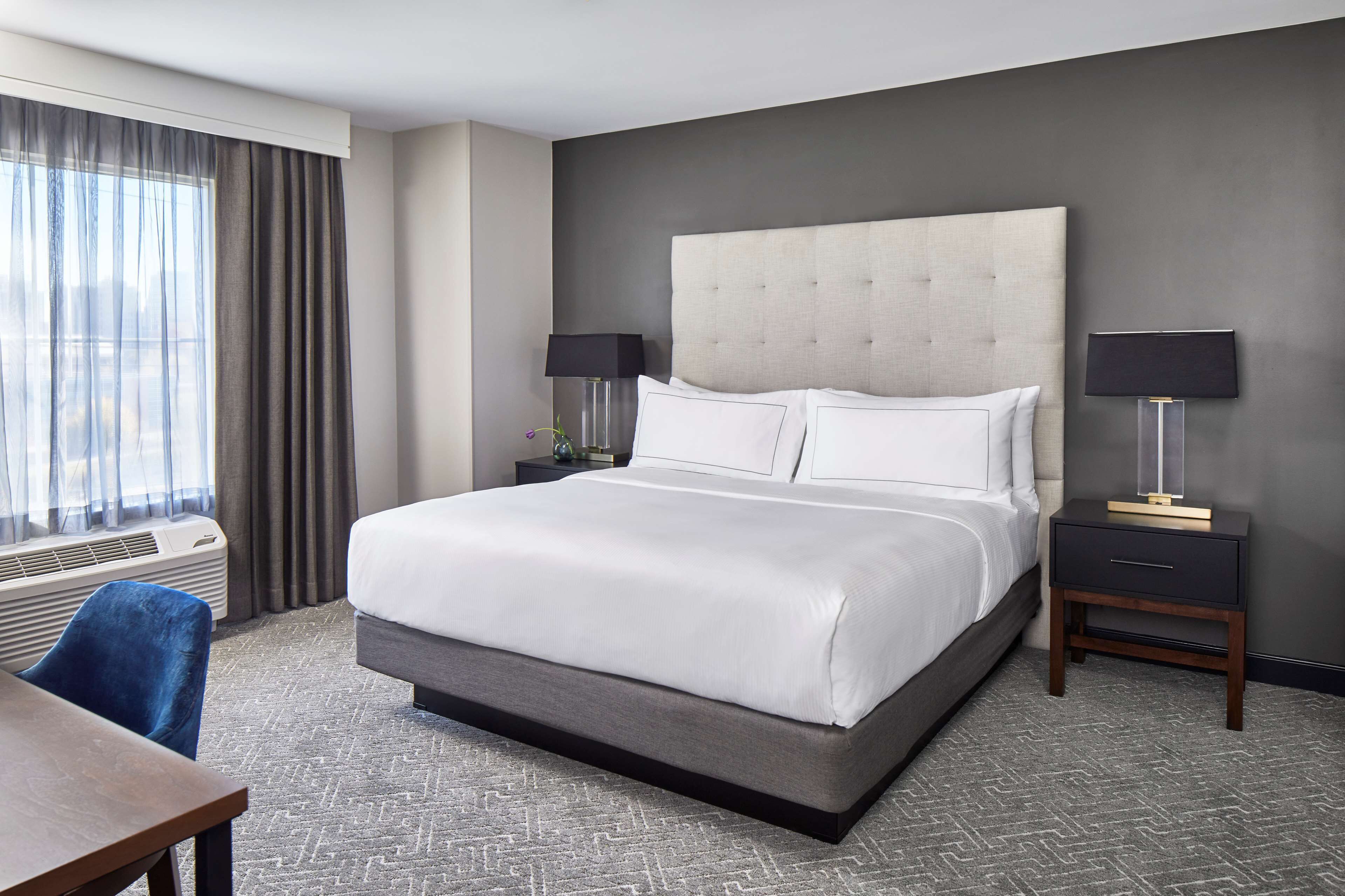 A hotel room with a large bed, two bedside tables, a desk, and a window with curtains.
