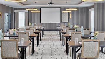 Un salón de conferencias con una pantalla grande, varias mesas y sillas dispuestas para reuniones.
