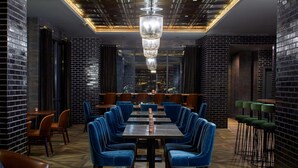 A restaurant with a brick wall, blue velvet chairs, and a chandelier.