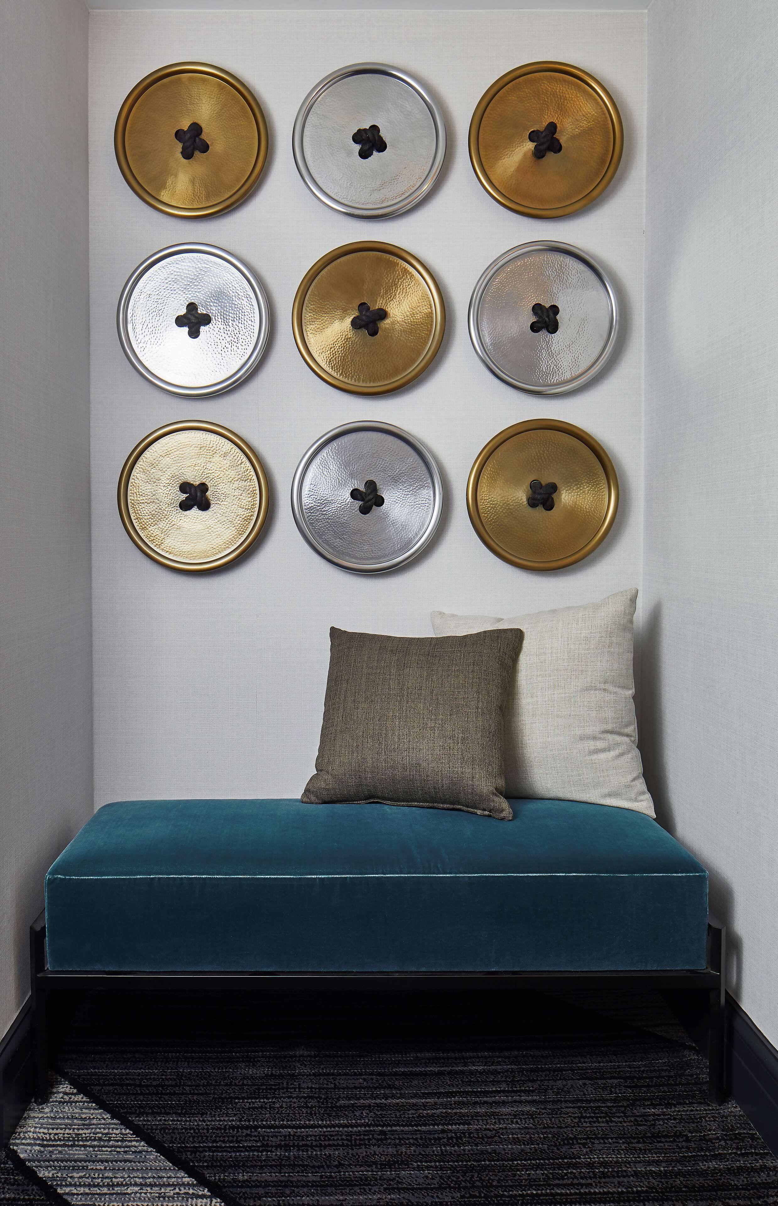 Una habitación con un sofá color turquesa, dos almohadas y una pared decorada con placas metálicas circulares.
