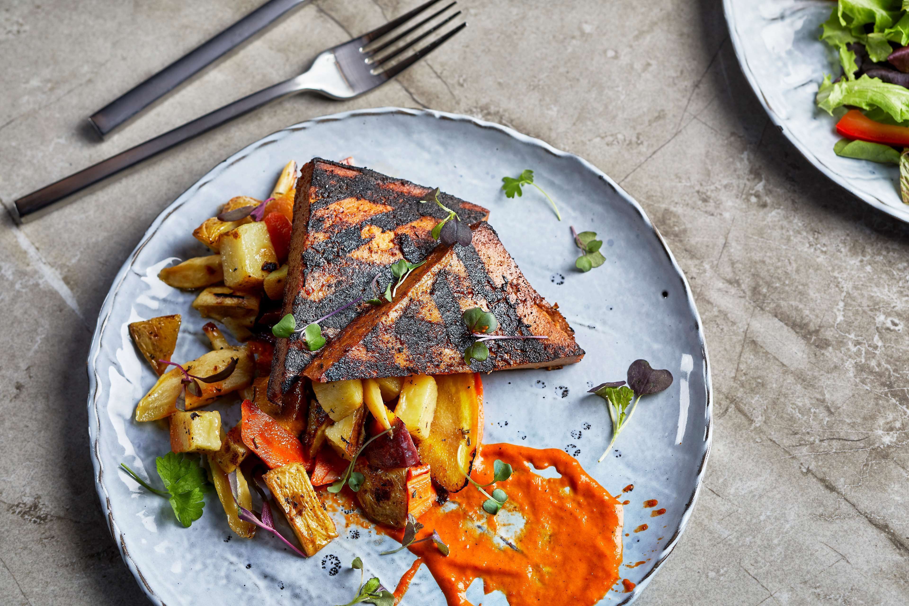 Une assiette comprenant du poisson grillé, des légumes rôtis et une sauce crémeuse.