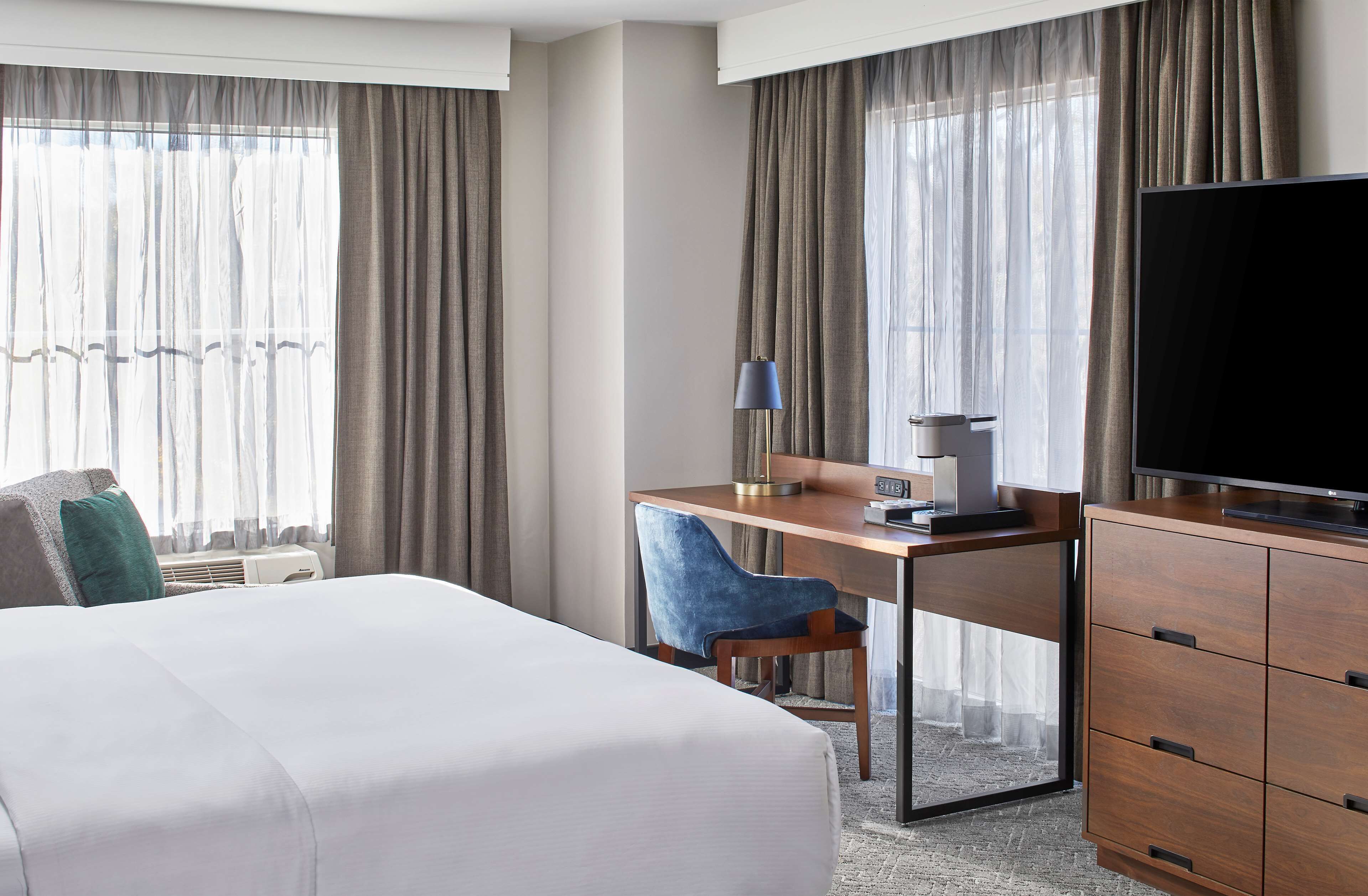 Ein Hotelzimmer mit einem großen Bett, einem Schreibtisch mit Stuhl, einem Fernseher und einem Kleiderschrank.