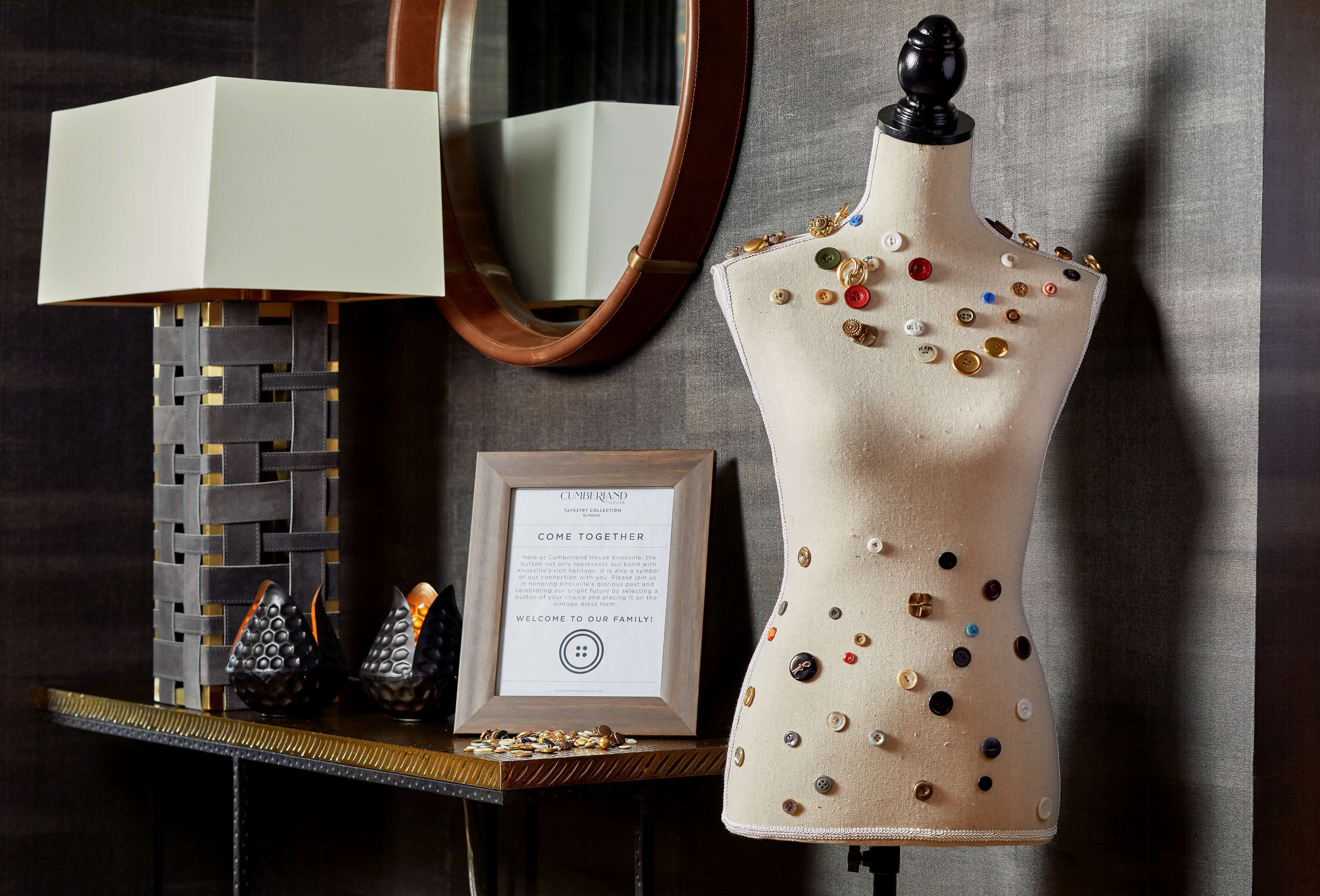 A mannequin with buttons, a framed sign, and a lamp on a table.