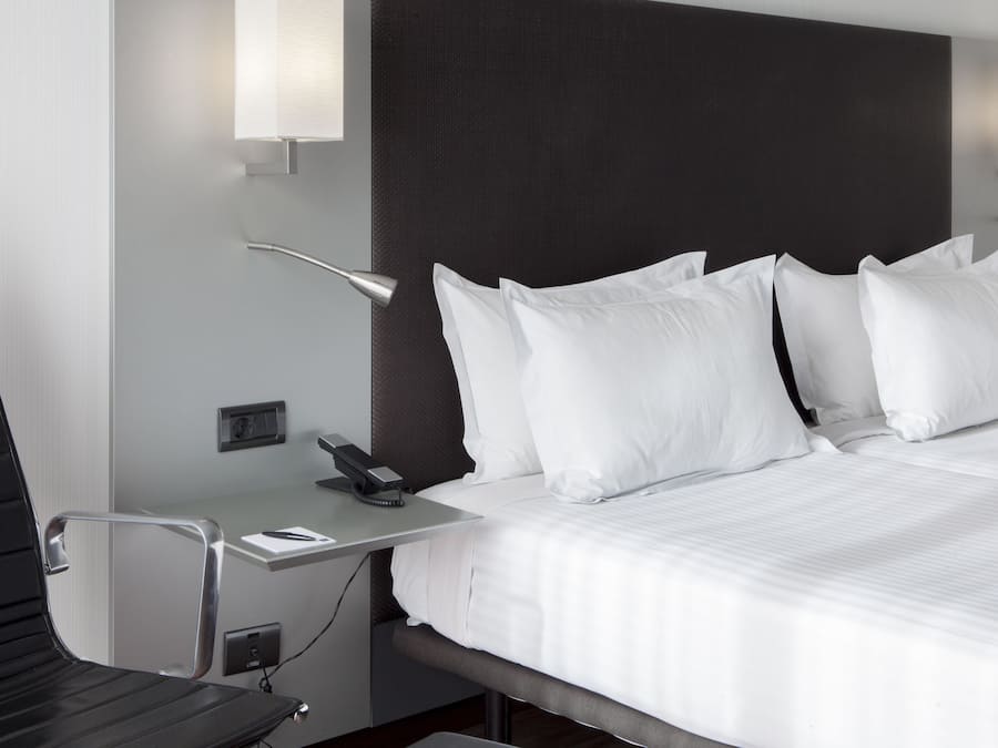 A modern hotel room with a large bed, a desk with a telephone, and a chair.