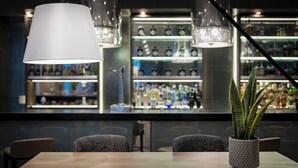 A bar area with a modern design, featuring a large hanging light fixture, shelves with bottles, and a potted plant on a table.