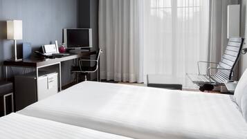 A hotel room with a bed, desk, computer, and a chair.