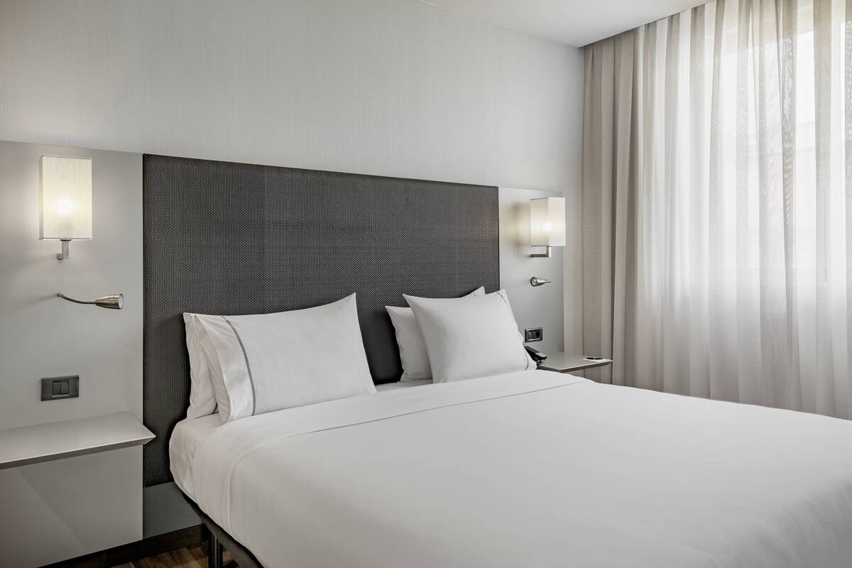 Een moderne hotelkamer met een groot bed, twee nachtkastjes en een hoofdbord met een structuurpatroon.