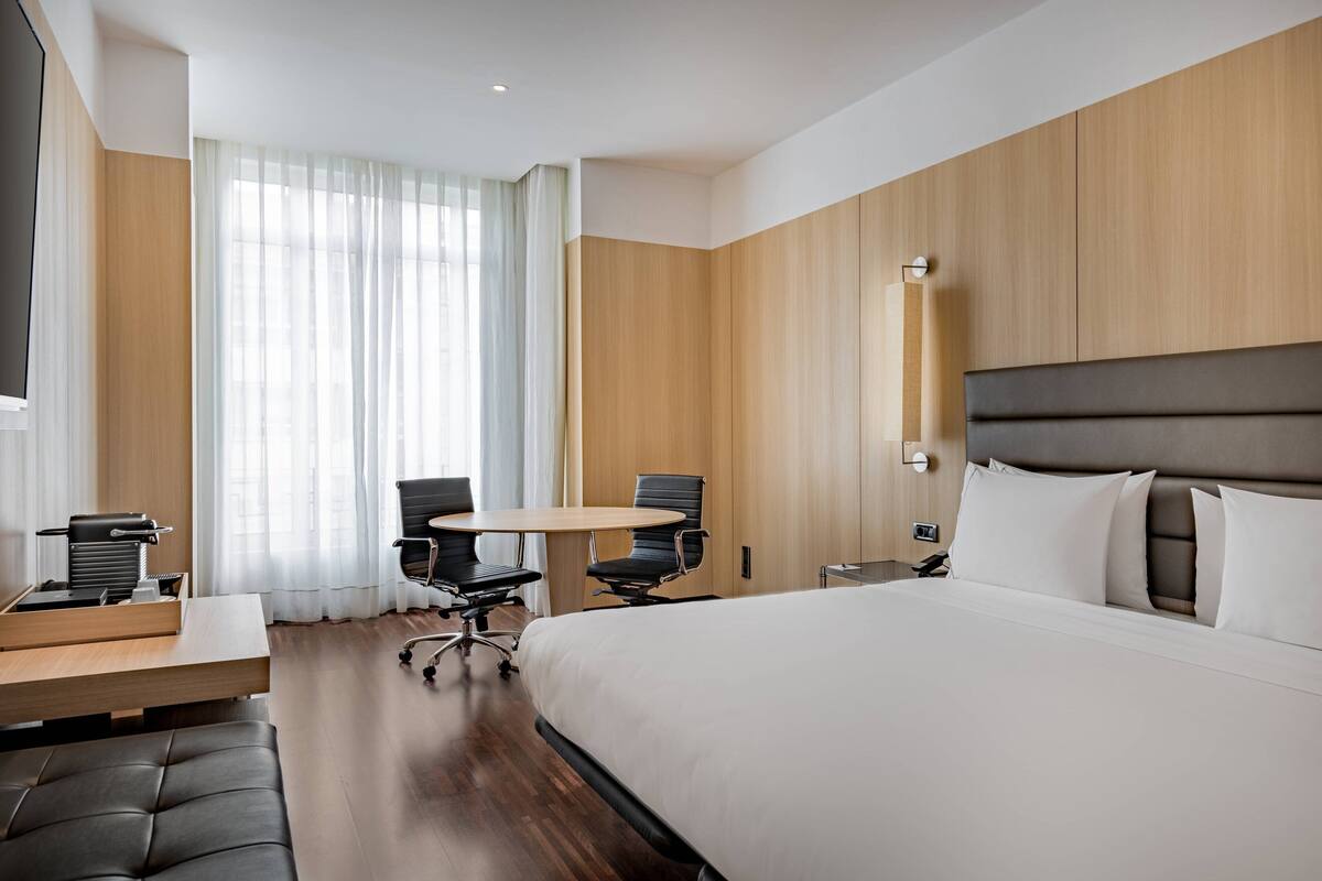 Een moderne hotelkamer met een groot bed, een bureau met stoel, een klein tafeltje en een televisie.