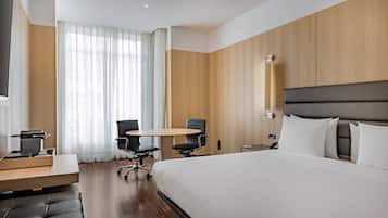 A modern hotel room with a large bed, a desk with a chair, a small table, and a TV.