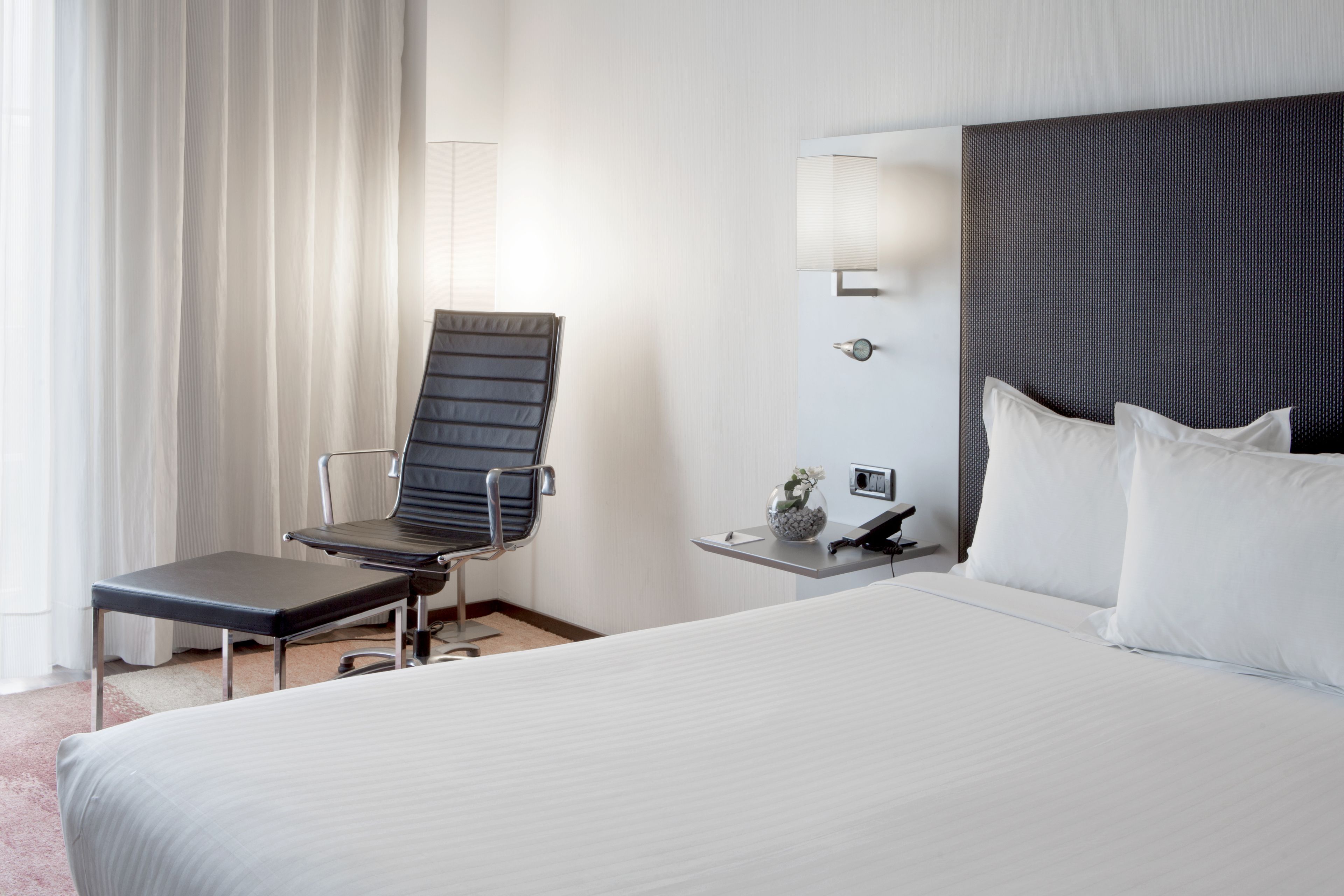 Een hotelkamer met een groot bed, een stoel, een nachtkastje met een lamp en een aan de muur bevestigde telefoon.