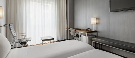 Une chambre d’hôtel avec deux lits, un bureau, une chaise, une télévision et une grande fenêtre avec des rideaux.