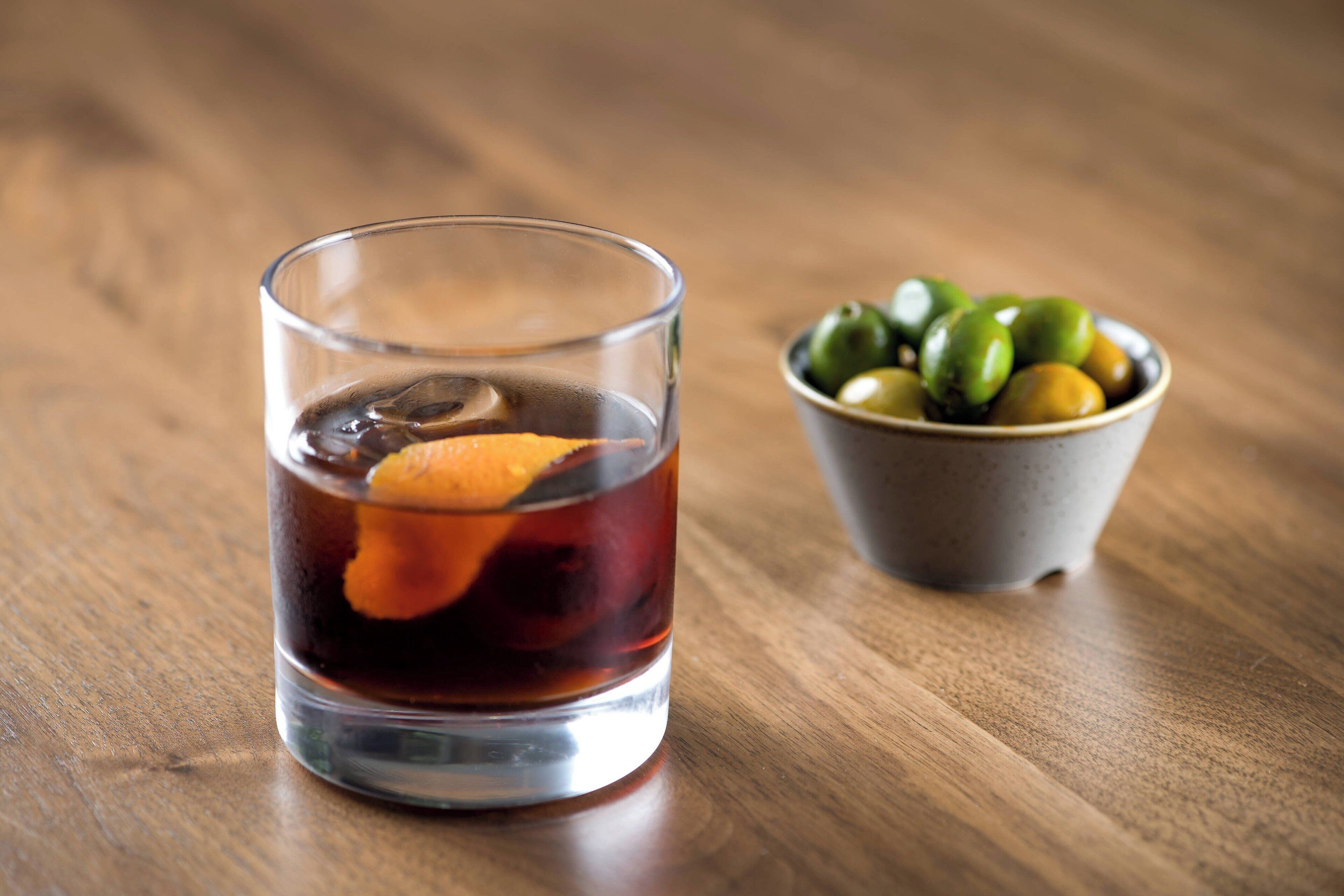 A glass of dark liquid with an orange slice on a wooden table.