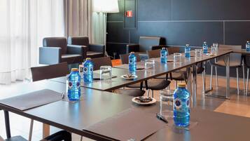Un salón de conferencias con una larga mesa, sillas, botellas de agua, vasos y una lámpara.