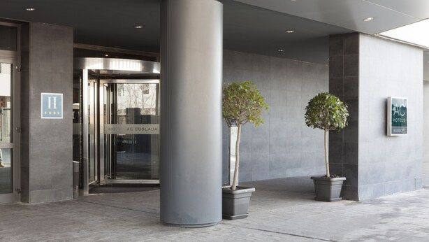 Entrada de hotel con puerta giratoria, dos macetas y un cartel que dice AC COSLAO HOTEL.
