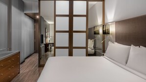 Una habitación de hotel moderna con una cama grande, un armario de madera, un baño con espejo y un escritorio pequeño.