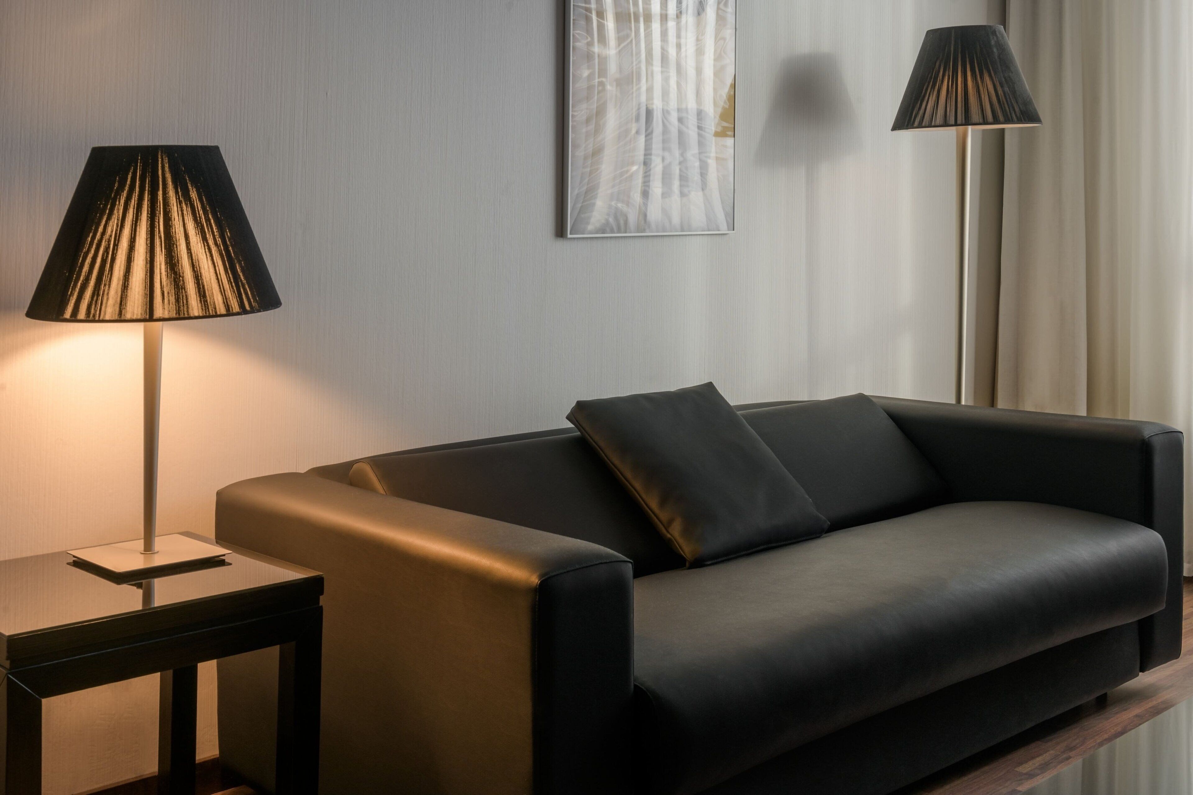 A modern living room with a black leather sofa, a side table with a lamp, and a floor lamp.