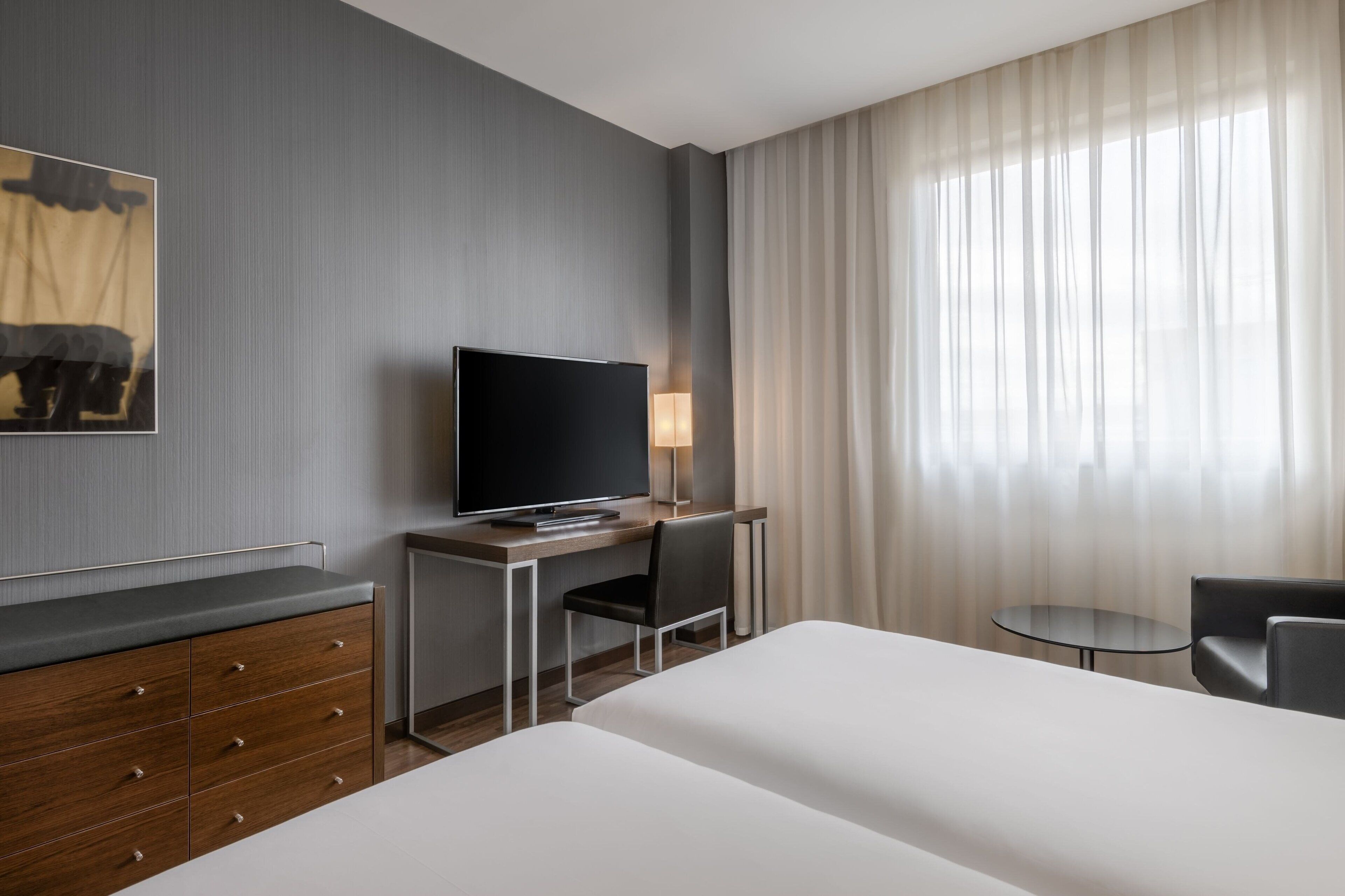 Ein Hotelzimmer mit einem Bett, einem Schreibtisch mit Fernseher, einem Sessel, einem kleinen Tisch und einer Lampe.