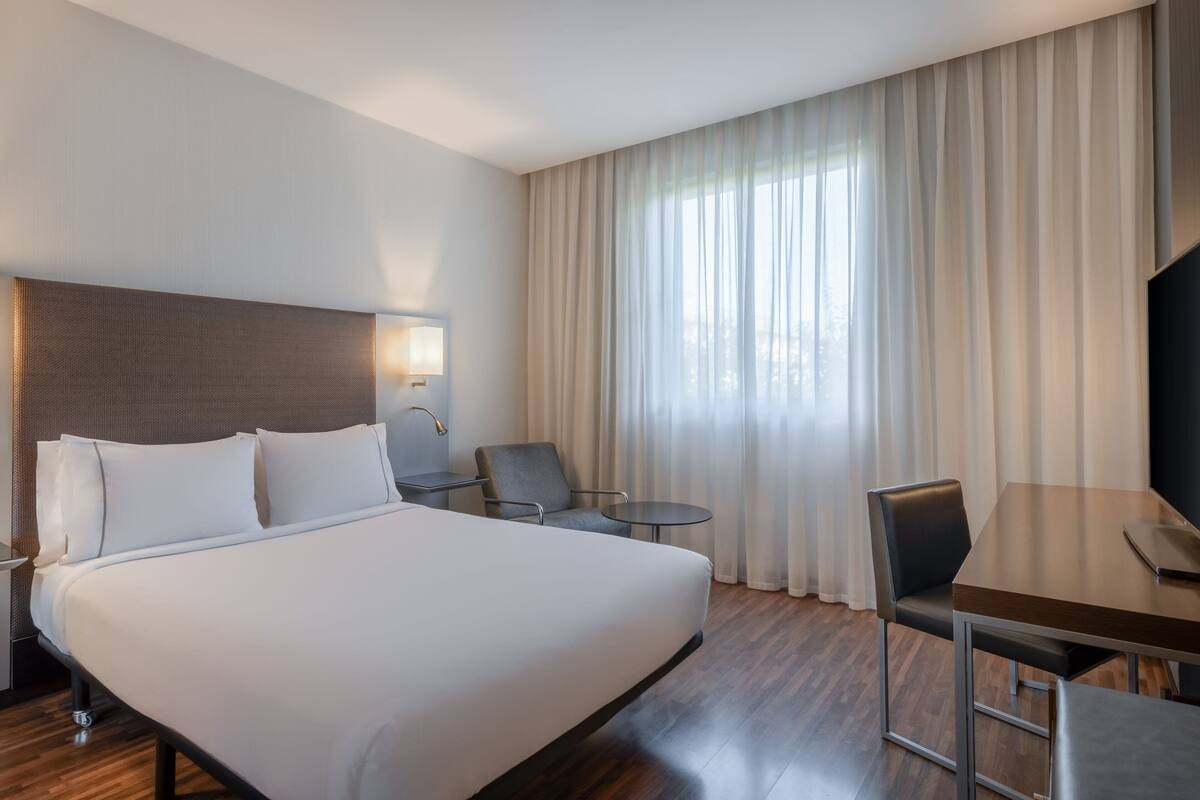 Habitación de hotel con una cama grande, un escritorio, una silla, una mesita y un televisor.