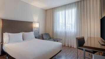 A hotel room with a large bed, a desk, a chair, a small table, and a TV.